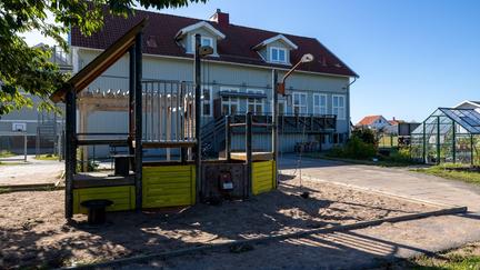 Bilden föreställer en byggnad och en uteplats med en klätterställning och ett växthus. 