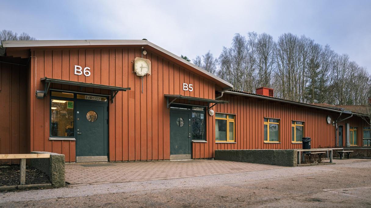 En röd skolbyggnad med två entrédörrar och en klocka på fasaden.
