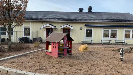 Bild på en gul byggnad med sandlåda och en röd lekstuga framför.