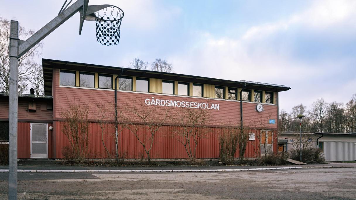 En basketkorg framför en röd skolbyggnad med texten Gärdsmosseskolan på fasaden.