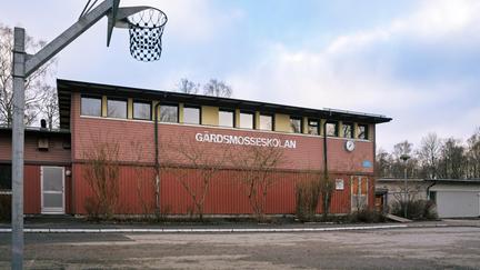 En basketkorg framför en röd skolbyggnad med texten Gärdsmosseskolan på fasaden.