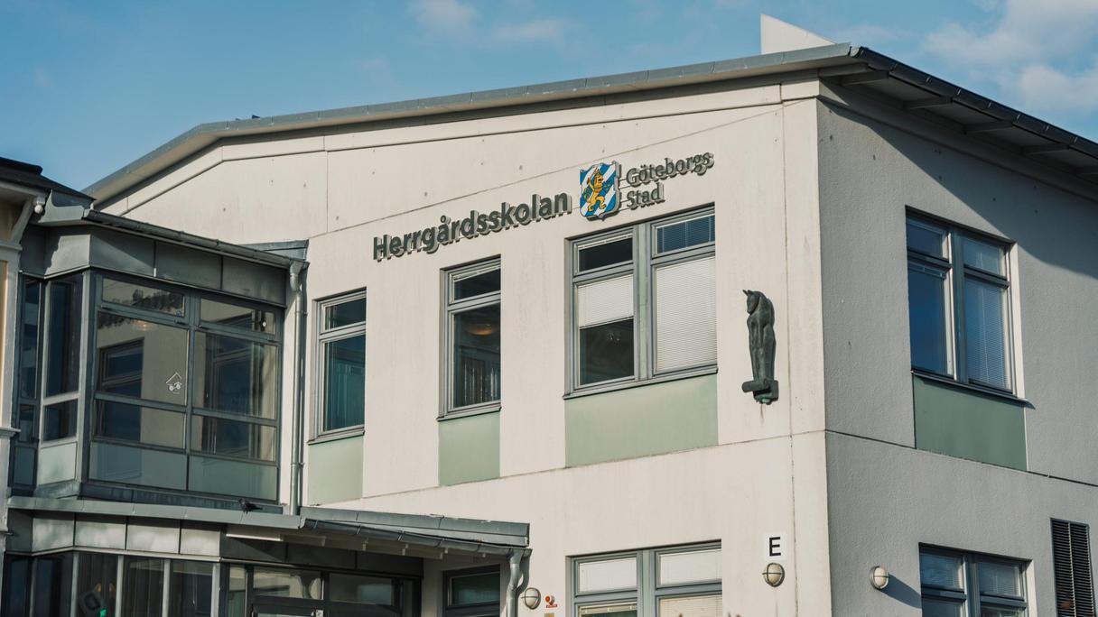 En stor vit skolbyggnad med texten Herrgårdsskolan Göteborgs Stad på fasaden.
