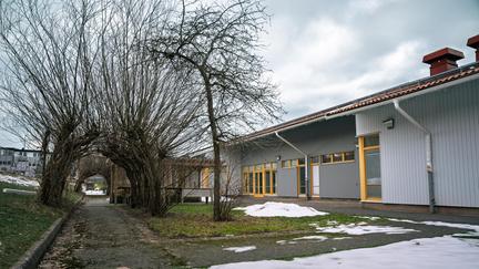 En väg utanför Hinnebäcksskolan med lutande träd som är formade som ett tak ovanför vägen. Snö och fler byggnader kan ses i bakgrunden.