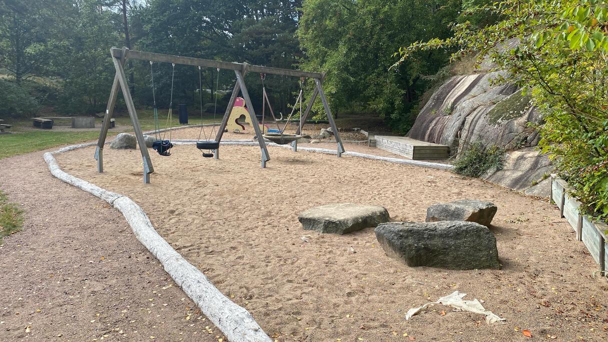 Runt lekplatsen finns träd som ger skugga och en berghäll. Lekredskapen är i områden med sand