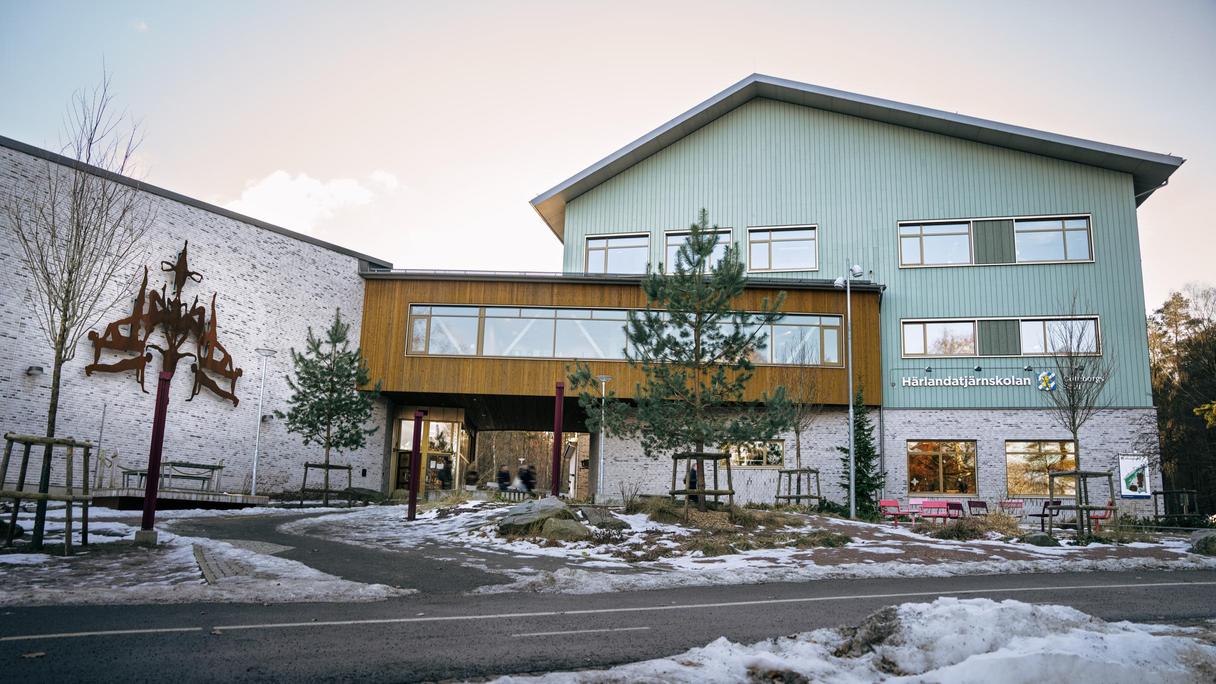 En skolbyggnad med texten Härlandatjärnskolan på fasaden med en väg framför.