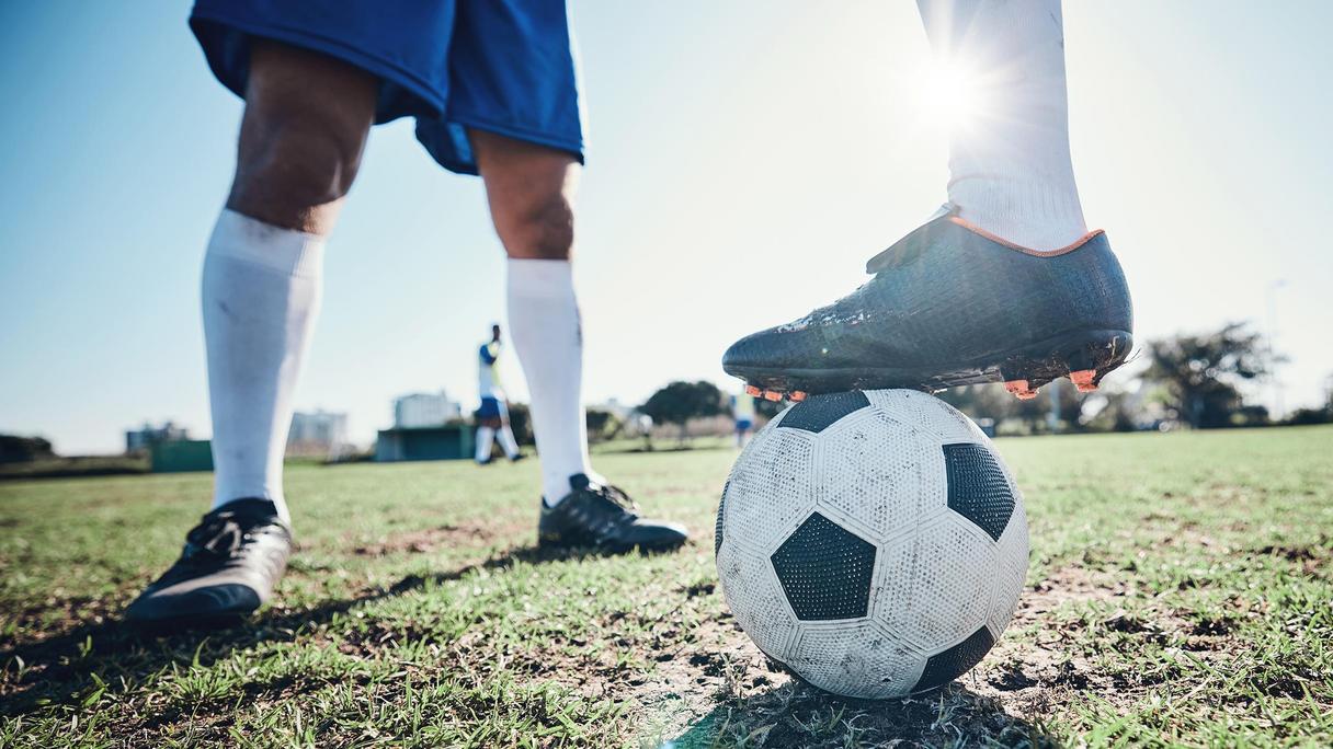 Två personer spelar fotboll på en gräsplan.