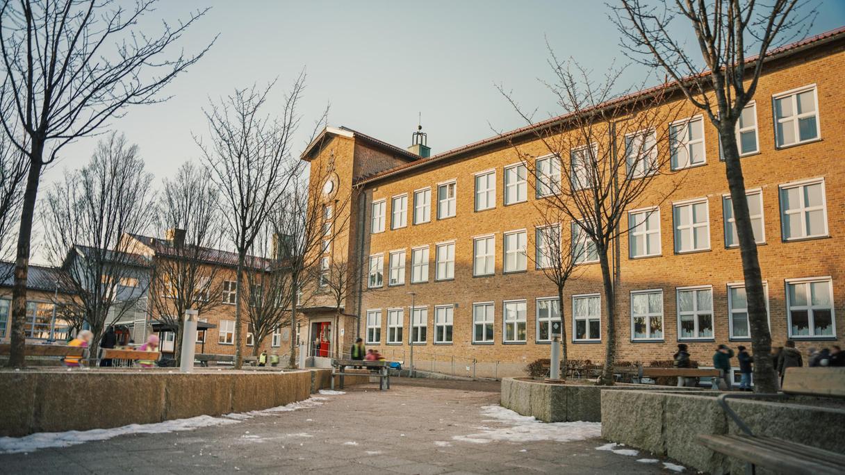 Johannebergsskolans skolgård med några personer och träd i bakgrunden.