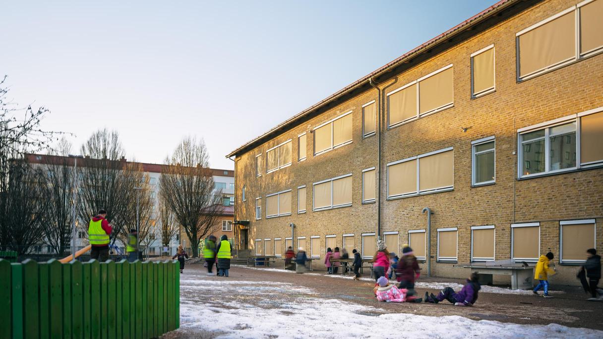 En lekställning och en grupp barn som leker framför en skolbyggnad.