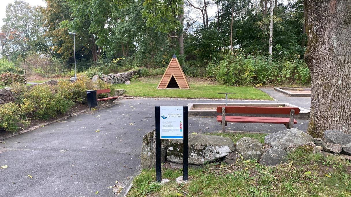 Runt lekplatsen är det många träd som ger skugga, finns även asfalterad yta och bänkar att sitta på