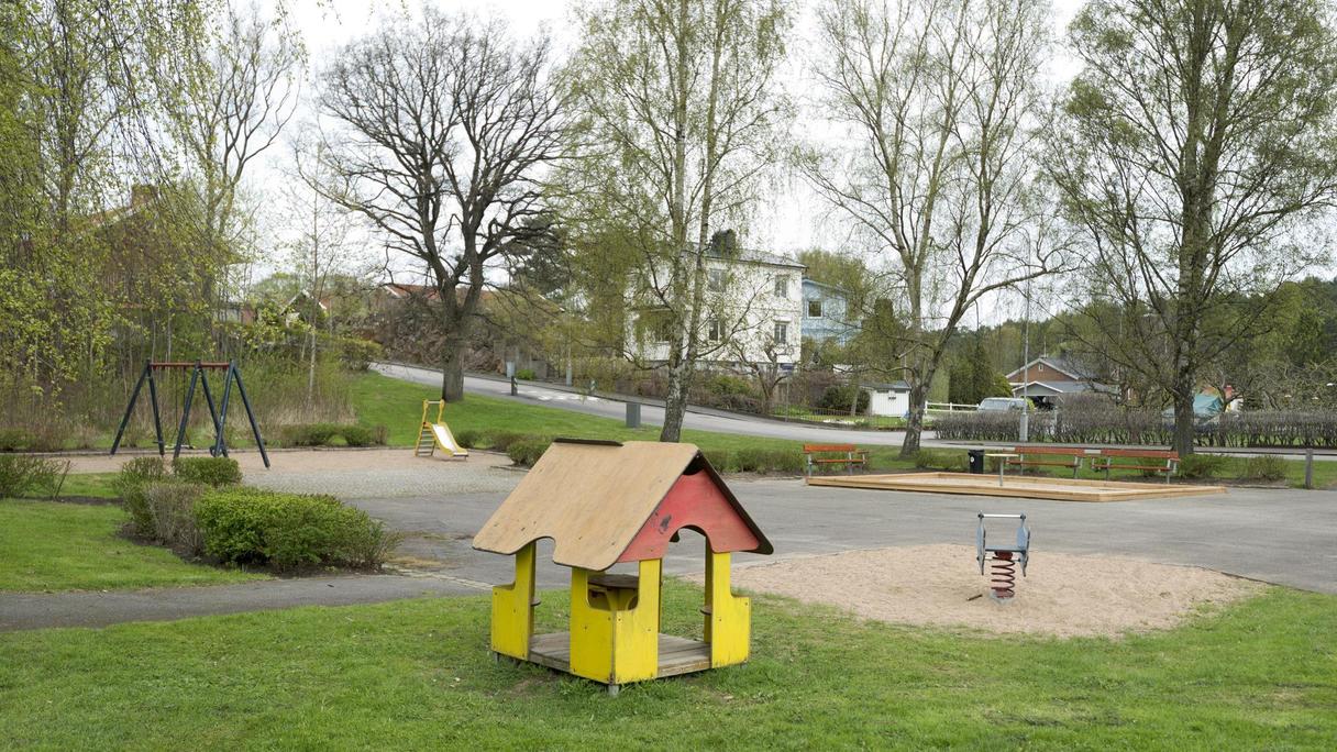 Yta av asfalt, gräs och sand med bland annat ett lekhus och gungdjur.