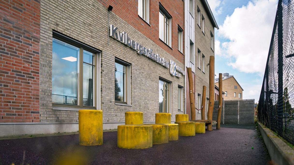 En rad gula pallar framför en skolbyggnad med texten Kvibergsnässkolan på fasaden.