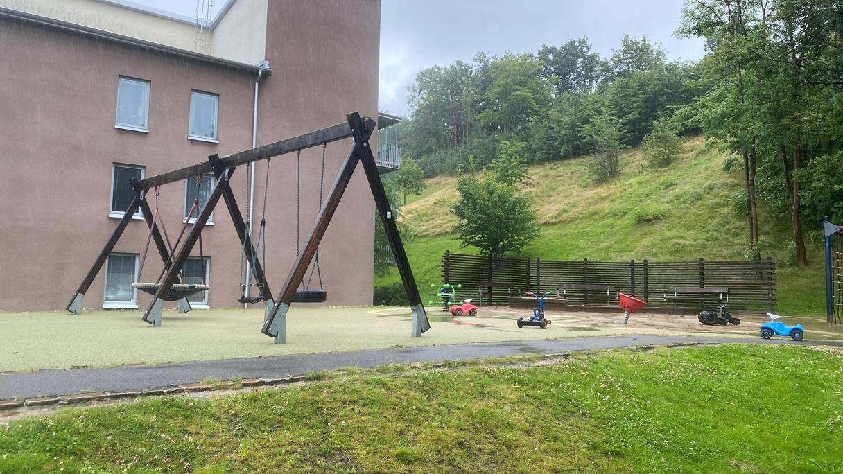 Lekplatsen ligger bredvid en grässlänt med träd som ger skugga