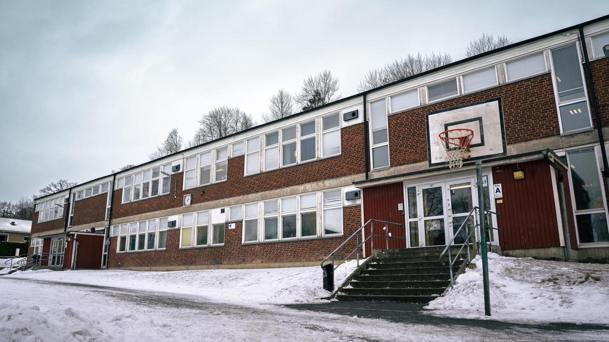 En entré till en skolbyggnad i rött tegel med en skolgård och en basketkorg framför.