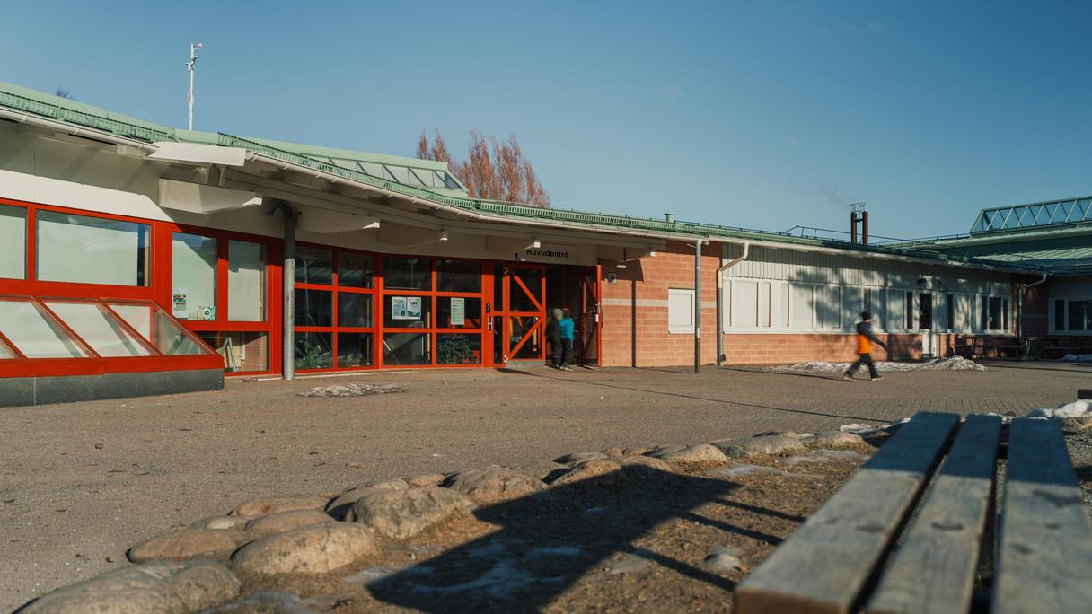 Lillebyskolans skolgård med några personer och en bänk i bakgrunden.