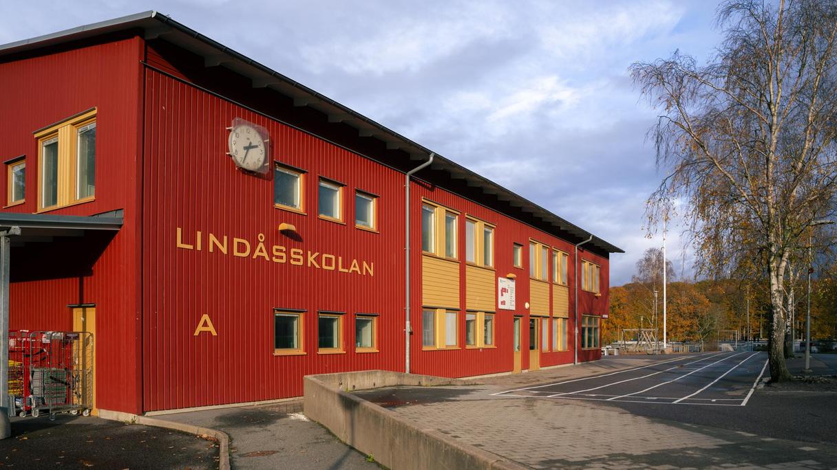 En röd skolbyggnad med en klocka och texten Lindåsskolan på sidan av den.