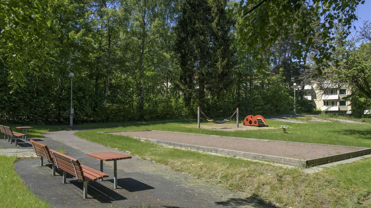 Yta av gräs, asfalt med bland annat en boulebana, en hängmatta och en liten rutschkana.