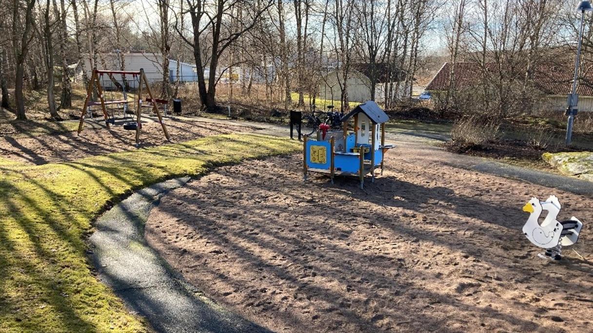 Yta av gräs och sand med bland annat en rutschkana och ett lekhus.