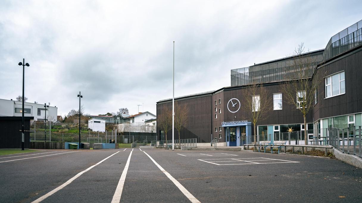 Långedragsskolans skolgård med några bänkar och träd i bakgrunden.