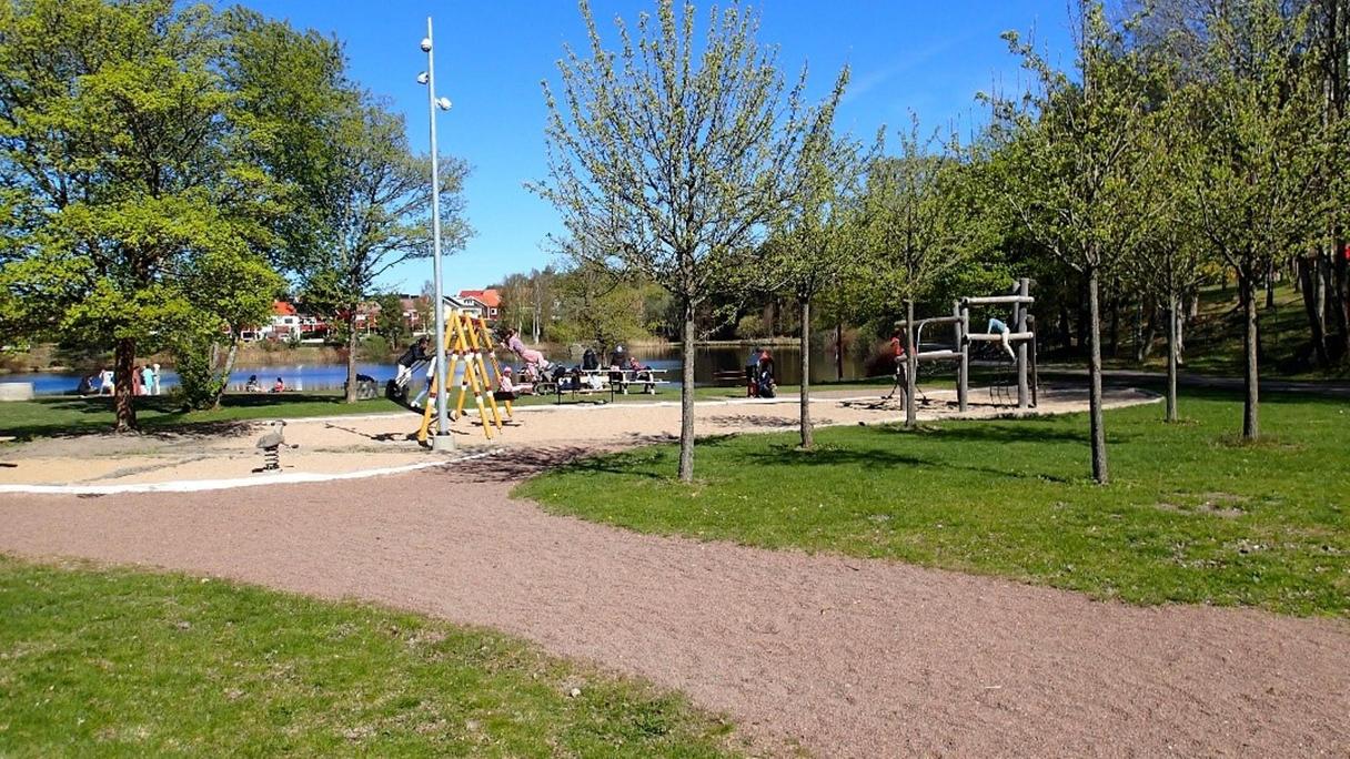 Stor gräsyta med en sandlåda och bollplaner. I sandlåda finns en gungställning och ett gungdjur.