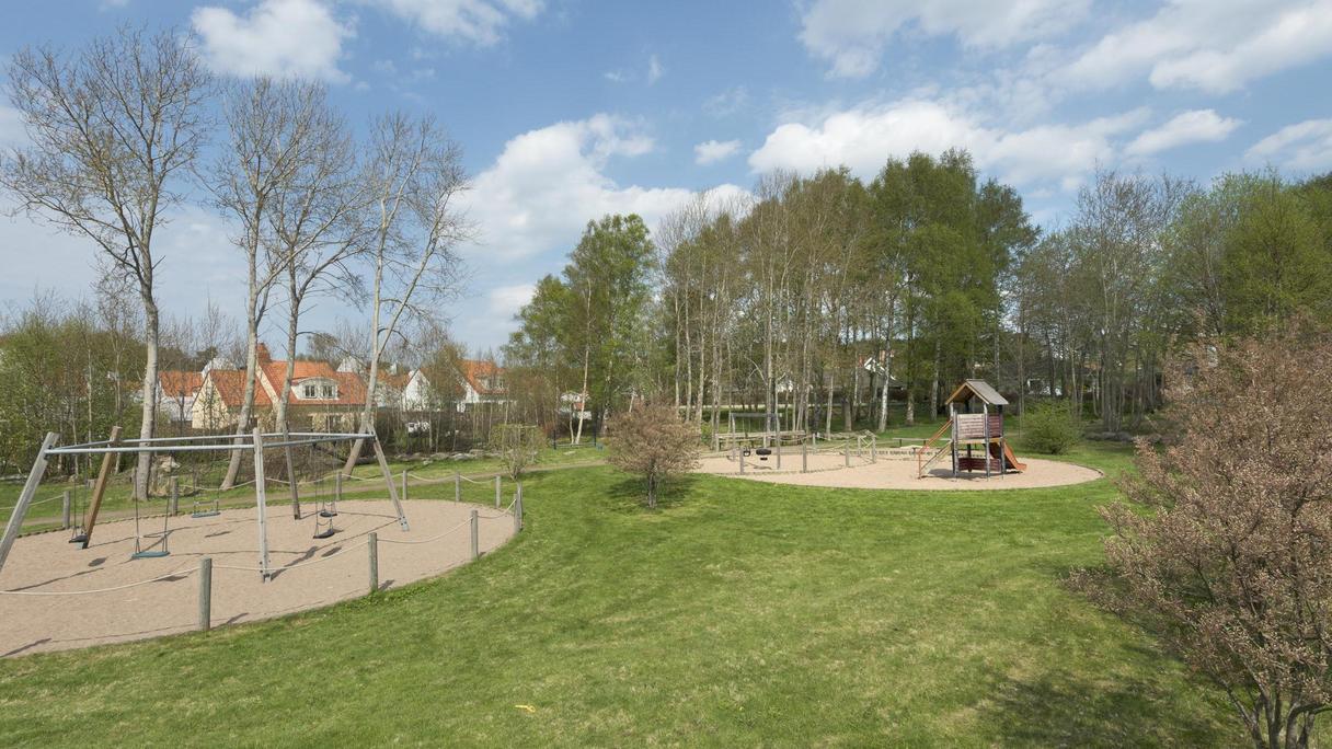 Område av gräs med två sandytor där bland annat en gungställning och en rutschkana finns.