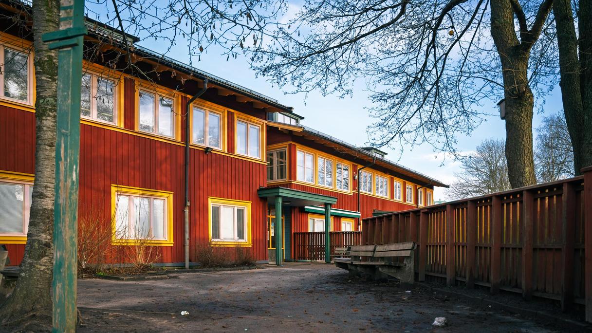 En röd skolbyggnad med entré och en bänk framför.