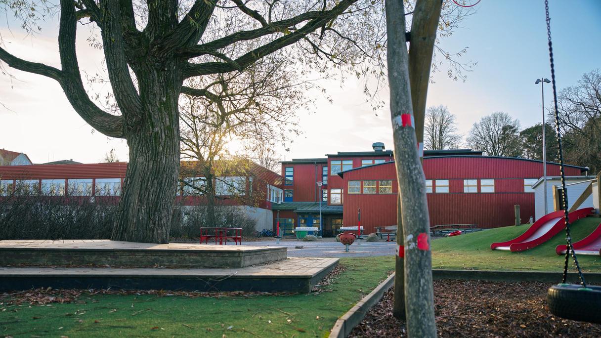 En skolgård med en rutschkana och en röd skolbyggnad i bakgrunden.