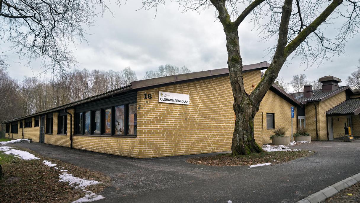 Olshammarskolans huvudbyggnad med en skylt och en skog i bakgrunden.