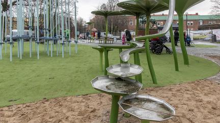 Yta av sand och konstgräs med bland annat en hög vattenlek med stuprör.