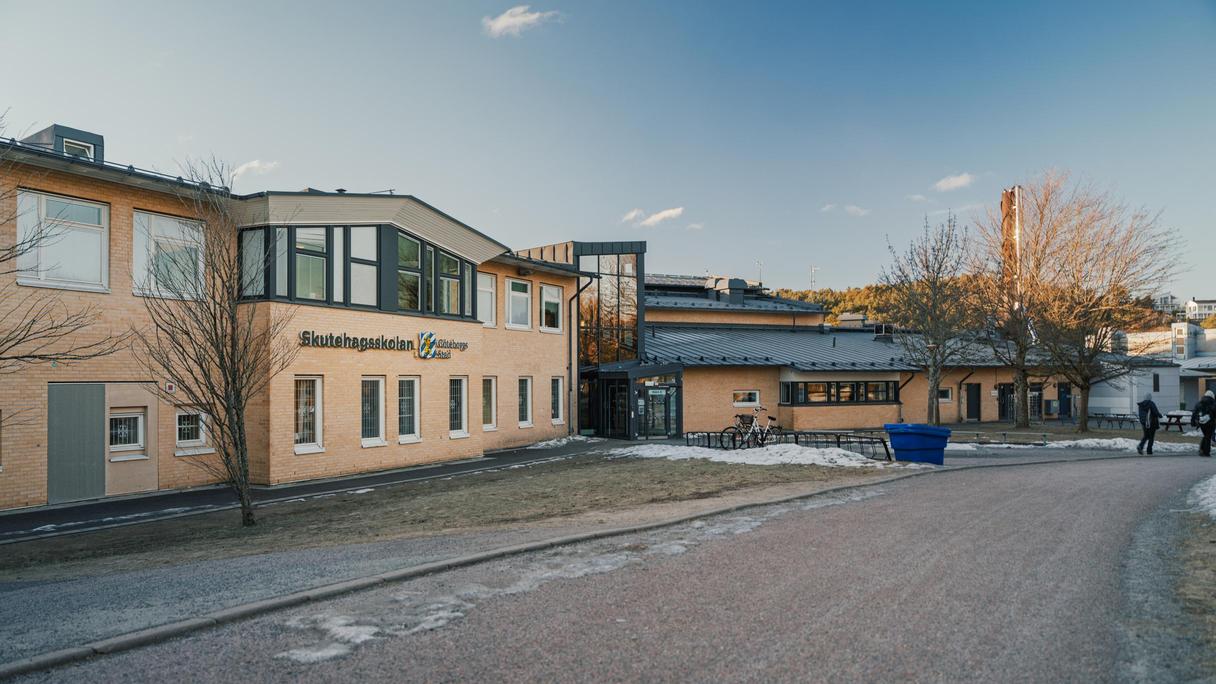 En skolbyggnad med texten Skutehagsskolan Göteborgs stad på fasaden med väg framför sig.