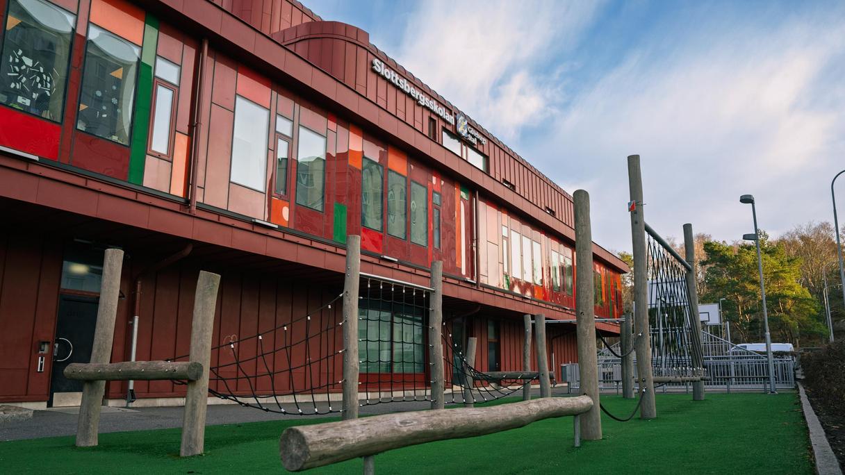 En röd skolbyggnad med en trappa och klätterställning på skolgården