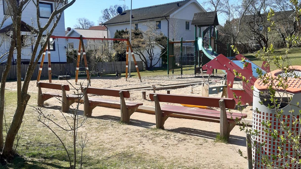 Lekplatsen ligger intill bostadshus, gräsmatta och bänkar runt om sandlådor med lekredskap