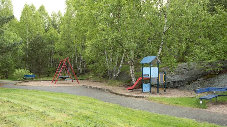 Yta av gräs, asfalt och en sandlåda med en gungställning och en klätterställning med rutschkana.
