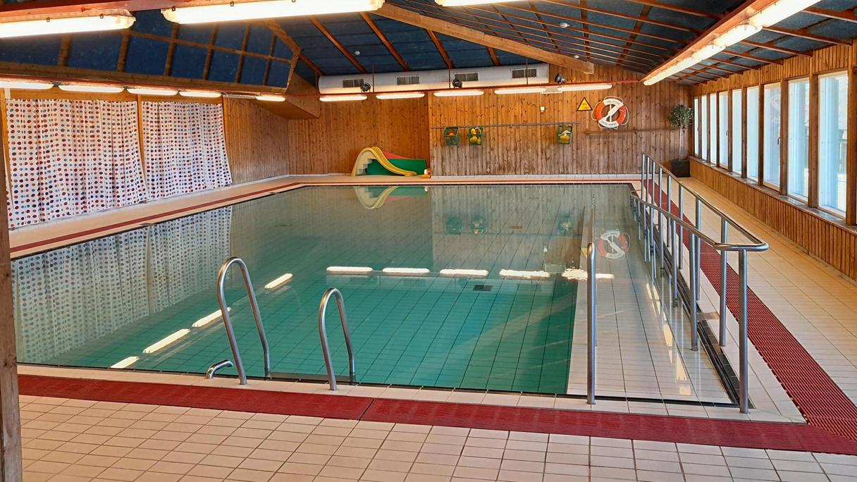 En inomhusbassäng i en byggnad med träväggar och fönster längs ena långsidan.