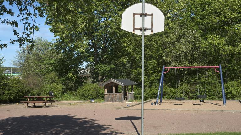 Yta av småsten och sand med bland annat en basketkorg och en gungställning.