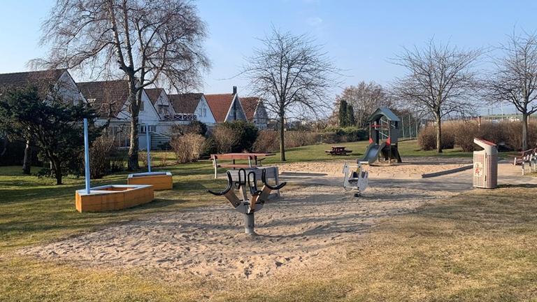 Lekplats med gräs och sand med lekbåtar, gungdjur, rutschkana och bänkar