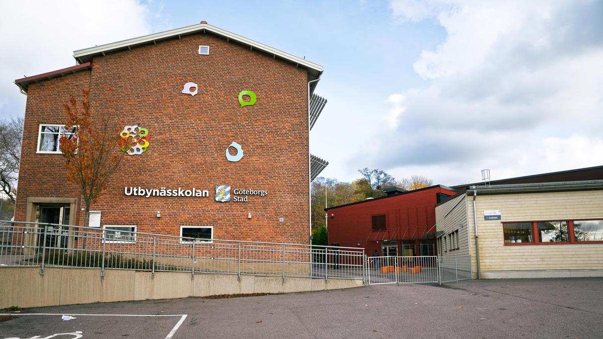 En skolbyggnad i tegel med en parkeringsplats framför