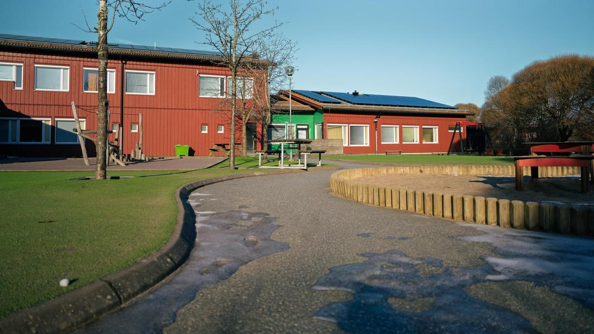 En väg som leder mot Älvegårdsskolan med skolans byggnader och en sandlåda i bakgrunden.