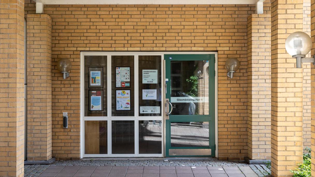 Ingången har glasdörrar med gröna kanter. Huset är byggt i gult tegel. 