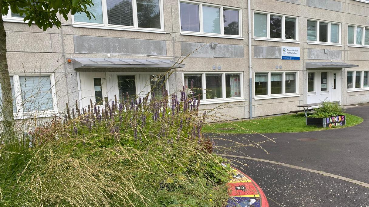 Ett grått höghus med planering framför. Vid ingången står en skylt med Öppna förskolan.