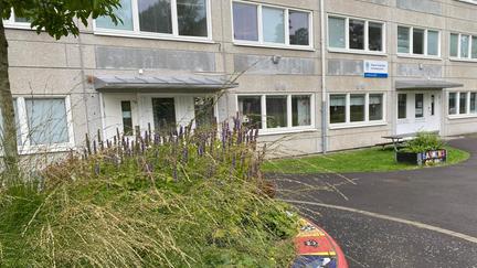 Ett grått höghus med planering framför. Vid ingången står en skylt med Öppna förskolan.