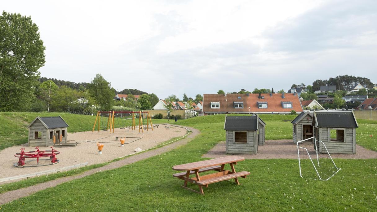 Yta av gräs och sand med bland annat en cykelkarusell, lekhus och gungställning.