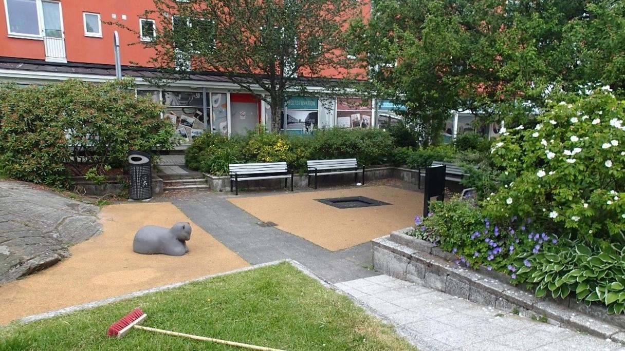 Ligger på torget med stenbelagt underlag med bänkar och buskar runt om