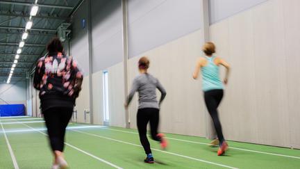 Tre personer med ryggarna mot kameran, springer på löparbanorna inomhus, 