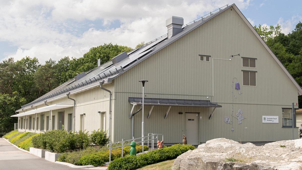 En beige förskolebyggnad med skog eller en dunge i bakgrunden.