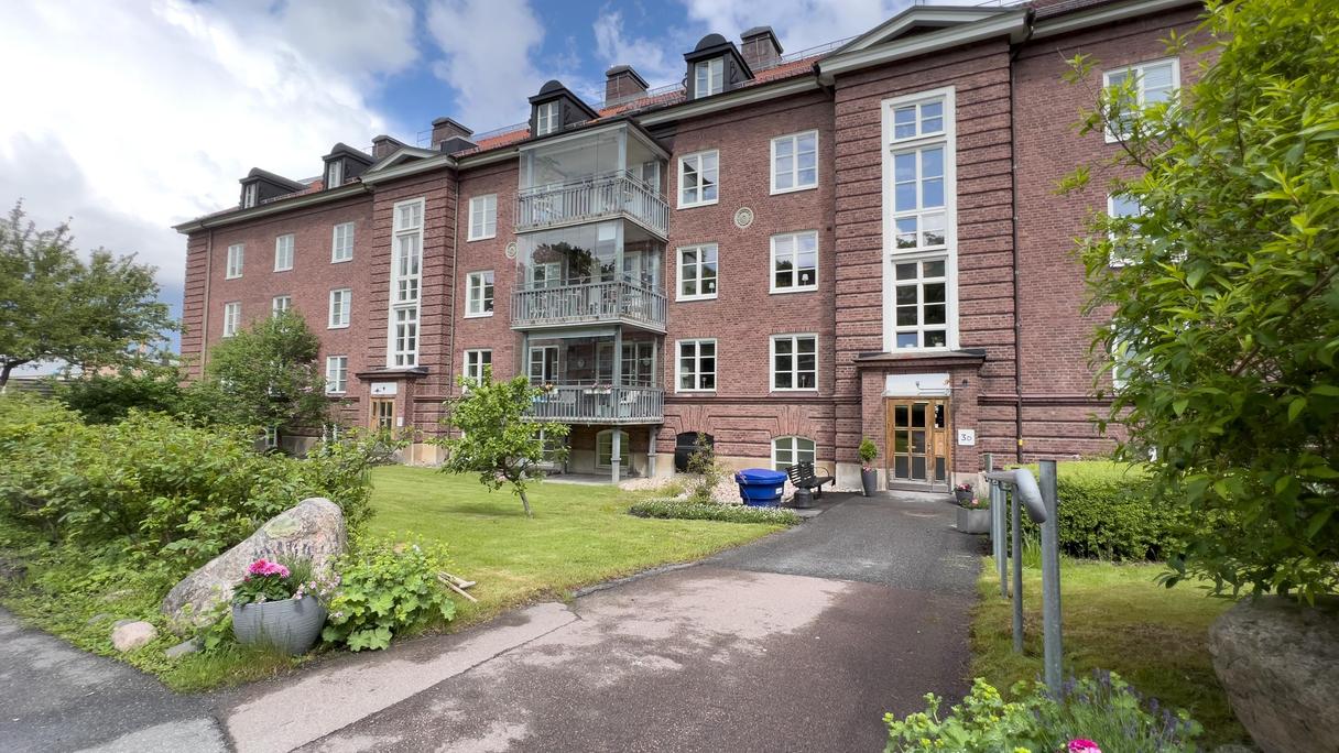 Tegelbrunt hus med en gång till entrédörren. Sommar.