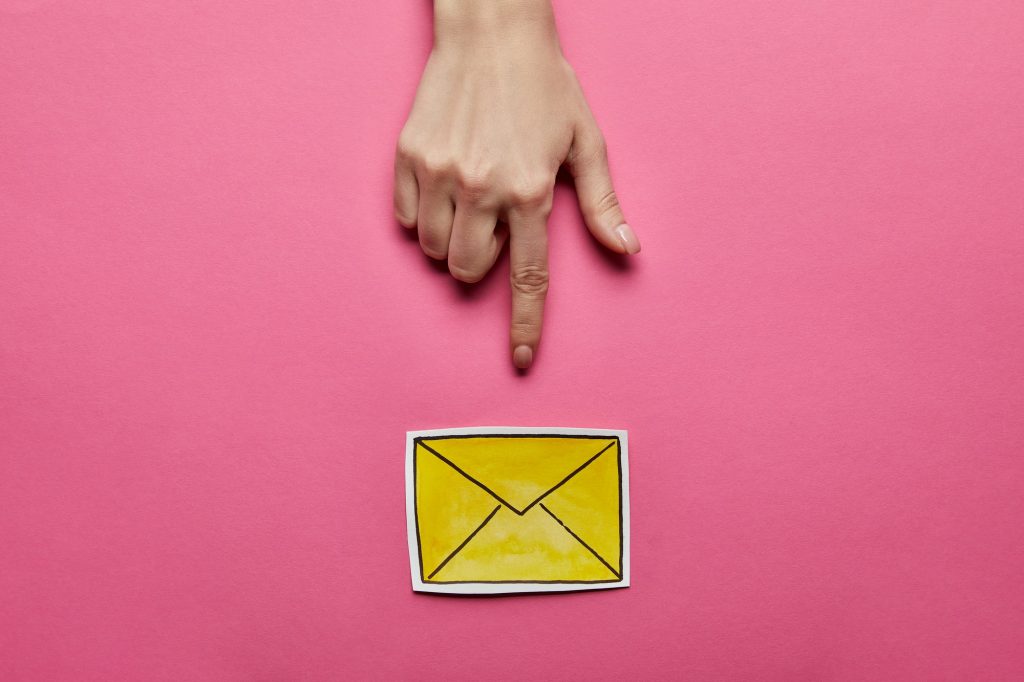 top view of hand pointing at yellow mail sign on pink background