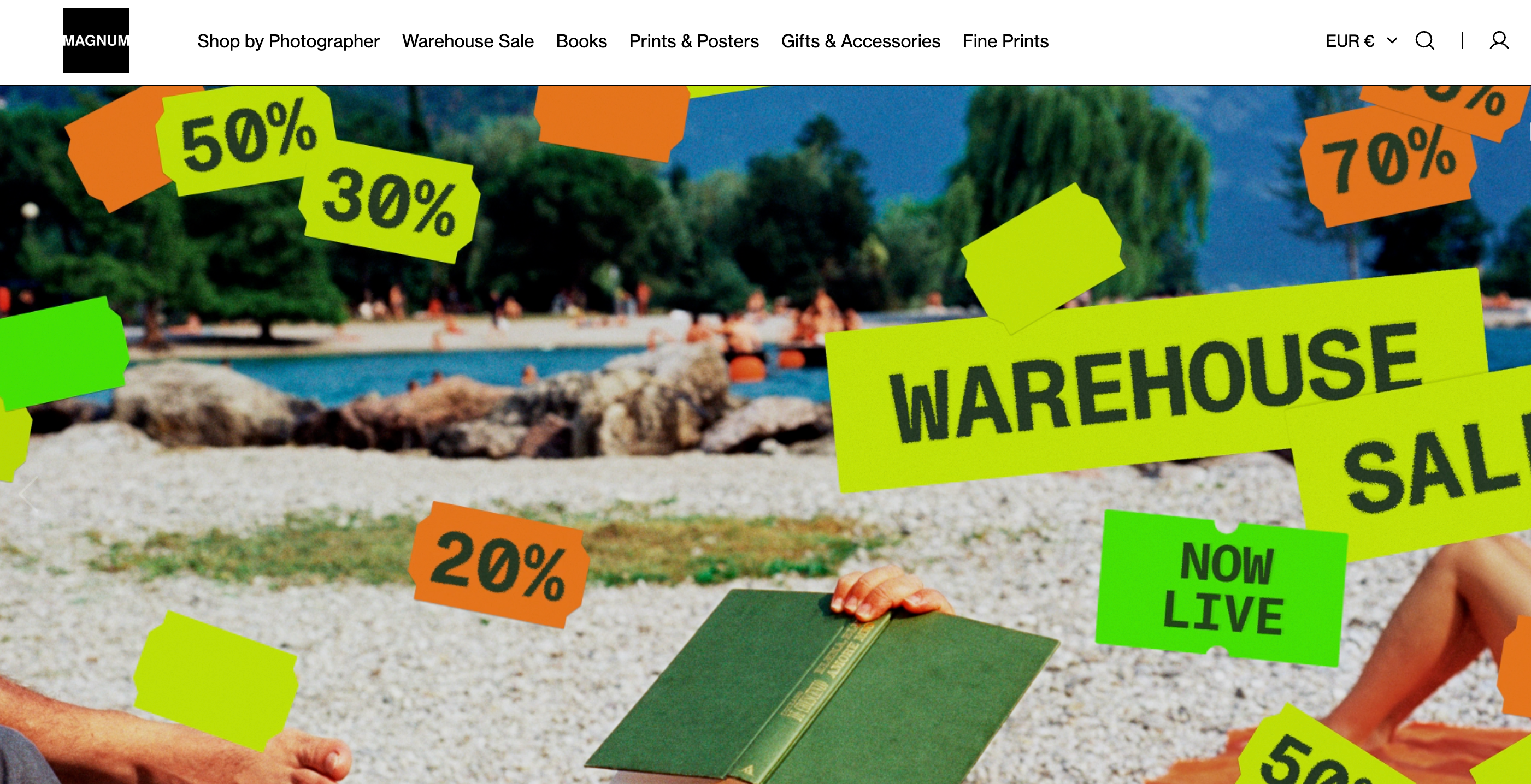 Homepage of Magnum Photos, a macrostock agency known for high-quality, rights-managed photography, featuring a warehouse sale banner with bright discount tags over a beach scene