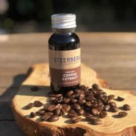 Bottle of Steenbergs Organic Coffee Extract, from the front view including label and lid on. Bottle on a piece of wood with a pile of coffee beans in front.