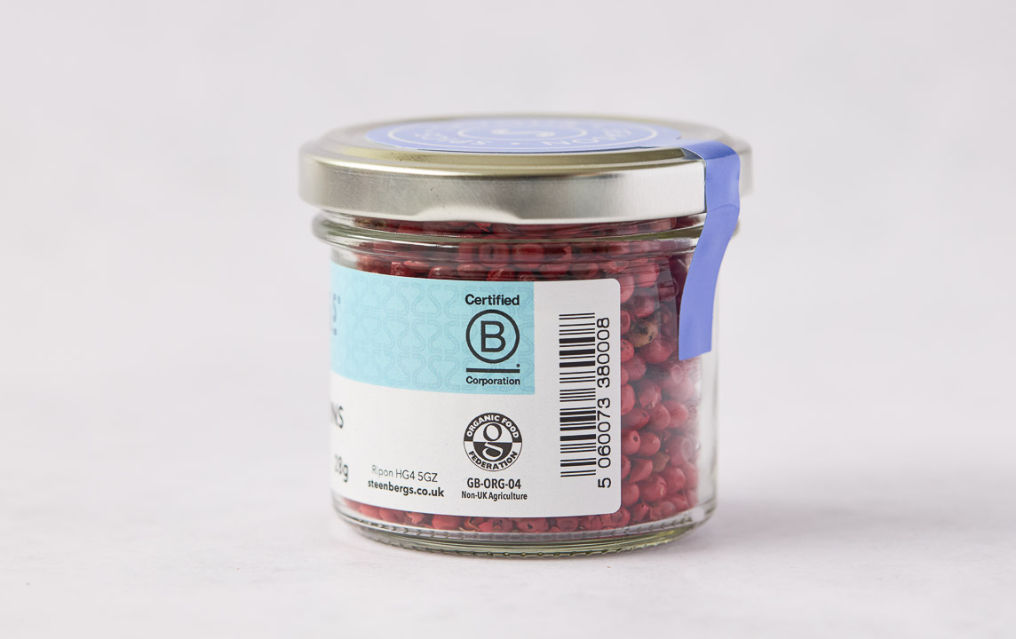 side view of Steenbergs organic pink pepper in jar showing organic logo and B-Corp logo, as well as pink peppercorns and the barcode